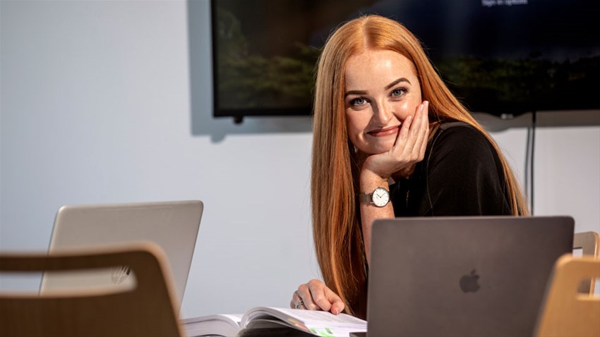 Kvinna sitter vid bord med en dator framför sig.