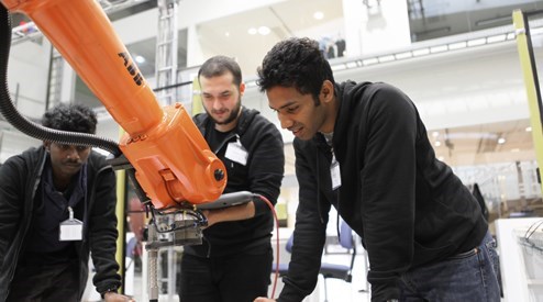 Tre personer står framför en robot i industrimiljö. Foto