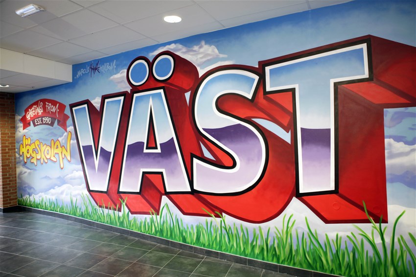 Foto på graffitimålning på en vägg innepå campus. Motivet är texten Högskolan Väst.