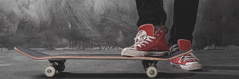 Bild på en ungdoms ben och skor. Står på en Skateboard. Foto