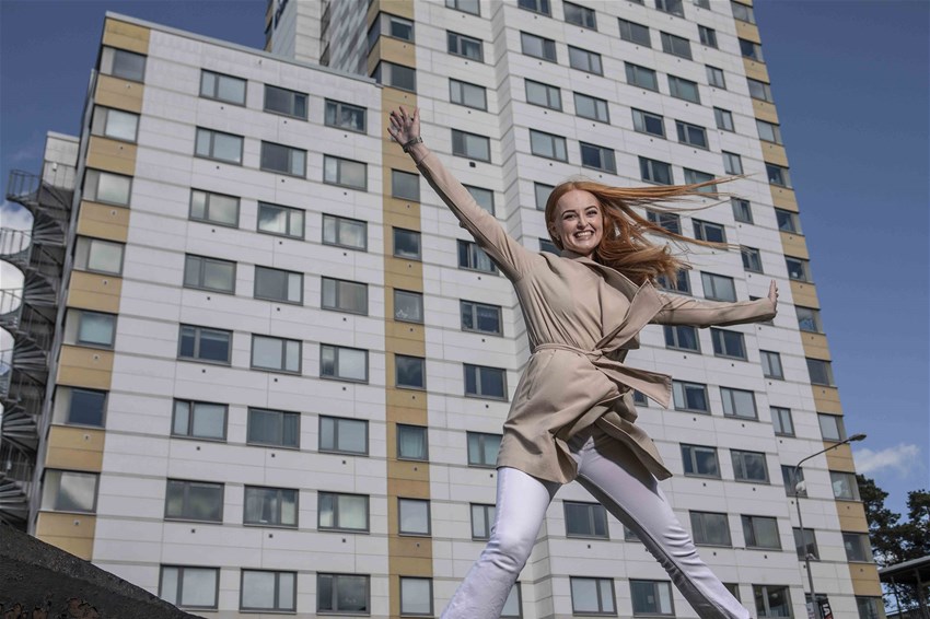 Student som hoppar i luften, sträcker ut armarna. I bakgrunden syns studentbostäder.