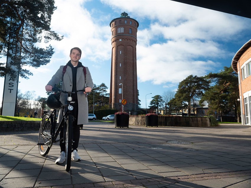 Student som leder en cykel framför Vattentornet i Trollhättan
