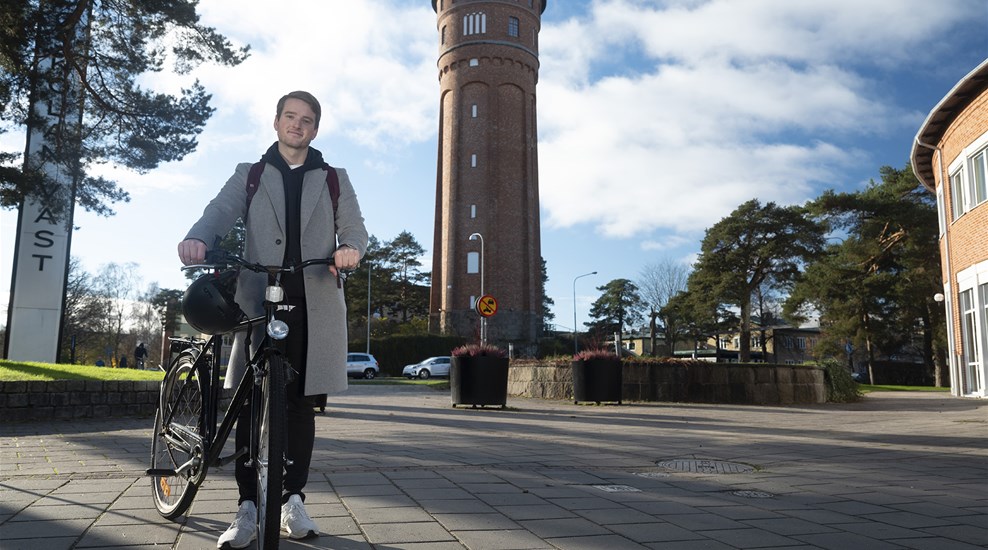 Student som leder en cykel framför Vattentornet i Trollhättan