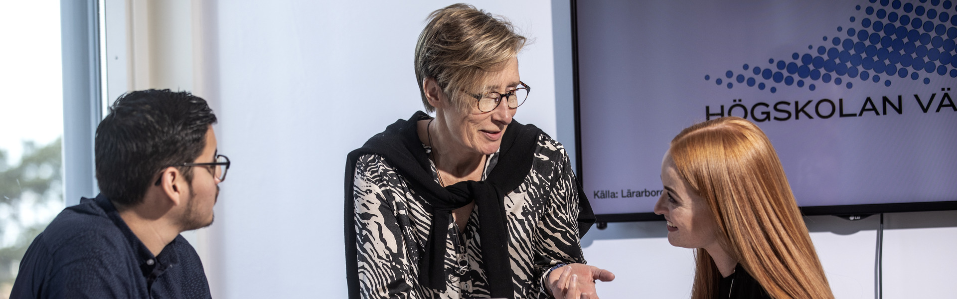 Studenter på Högskolan Väst sitter med varsin dator i ett klassrum och får hjälp av en lärare.