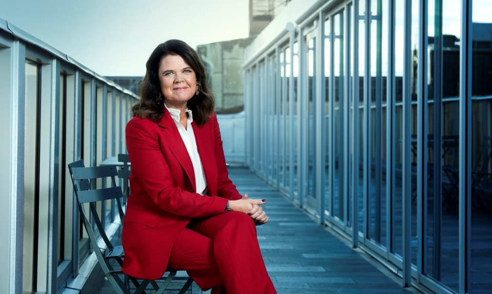 Moderatorn Anna Dyhre sitter på en stol utanför en byggnad. 