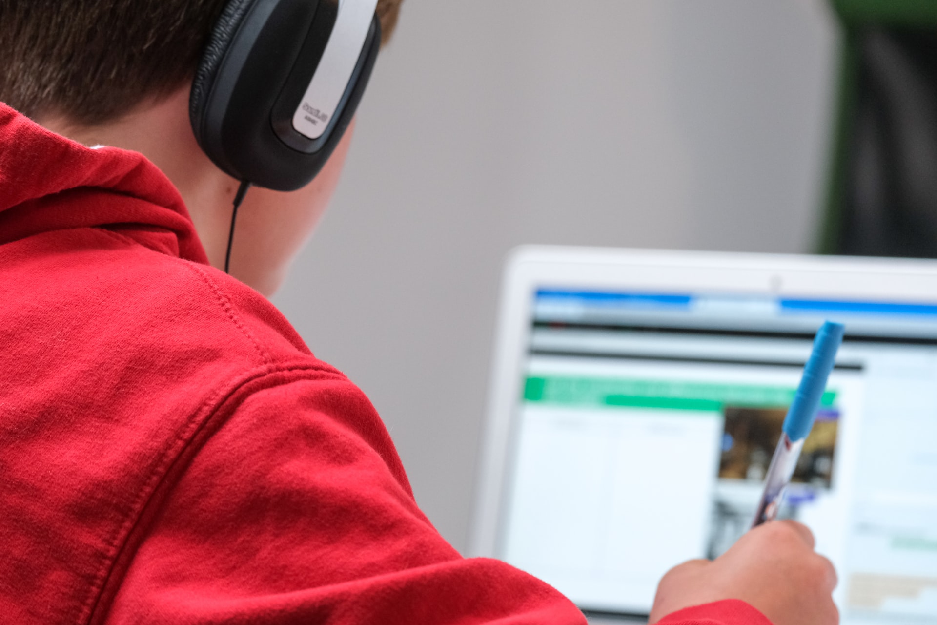 Pojke bakifrån sittandes med hörlurar och dator i skolmiljö