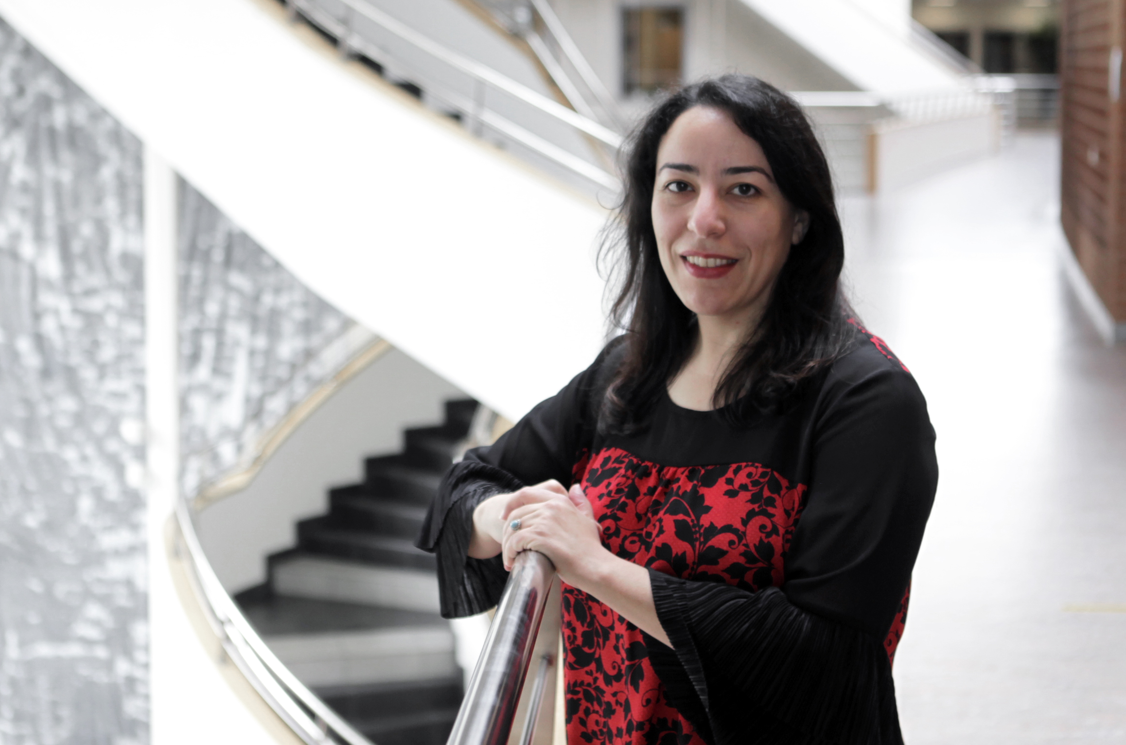 Samira, a woman, standing by a staircase. 