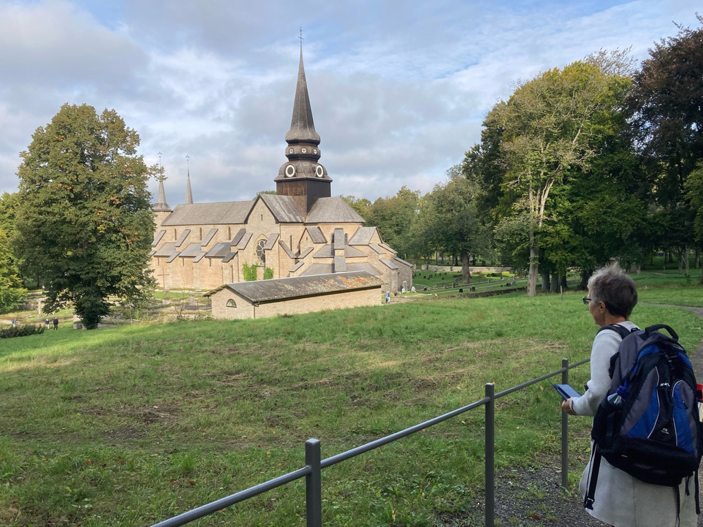 En människa tittar på en kyrka. Omgivande kyrkogård med gräs och träd.