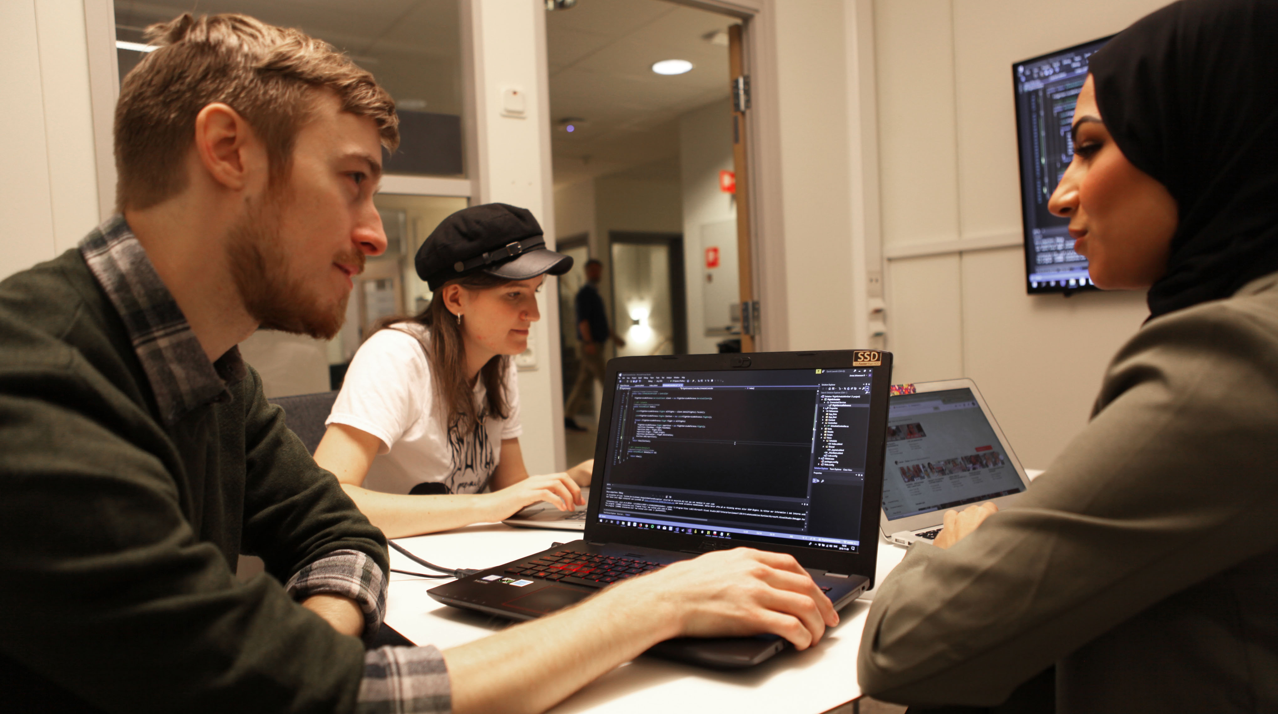 Tre studenter sitter i ett gruppgrum med datorer. Foto